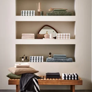 Op een badkamerplank liggen Vandyck Verona Stripes Handdoek Desert-handdoeken in aardetinten, naast vazen en een houten bank.