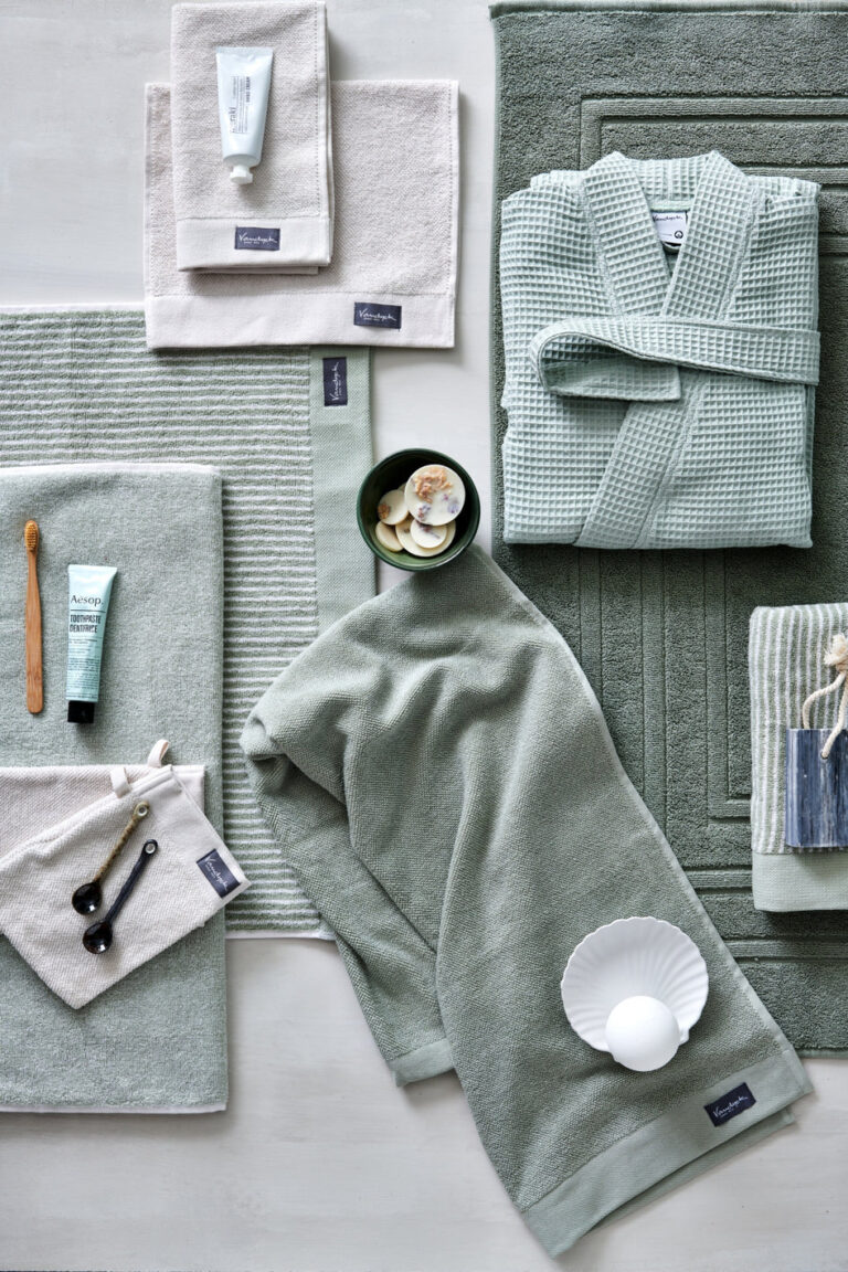 Netjes opgestapeld saliegroen en beige badlinnen, zoals de allerbeste handdoeken van topkwaliteit, zorgen voor een rustgevende spa-sfeer.