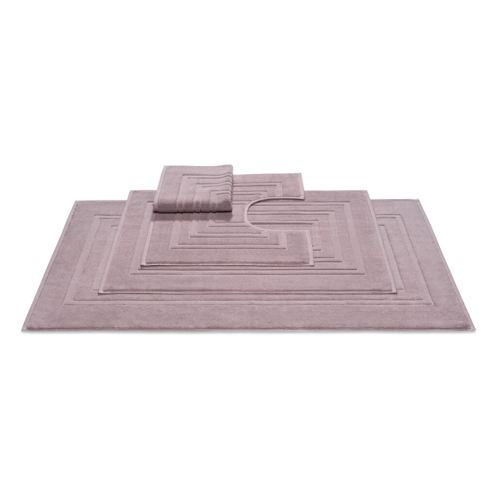 De Vandyck Houston badmatten set in mauve bestaat uit drie mauvekleurige badmatten met een geometrisch rechthoekig patroon, waarvan er één is voorzien van een handige uitsparing voor rond het toilet.