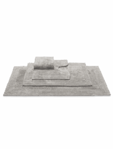 De Vandyck Scala Luxury badmat Stone is een stijlvolle, lichtgrijze badmat die netjes opgestapeld ligt naast andere matten.