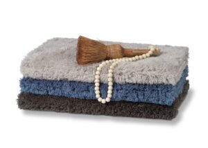 Op de Vandyck Toronto-badmat in Vintage Blue liggen grijze en donkergrijze handdoeken, een houten massageborstel en een kralenketting.