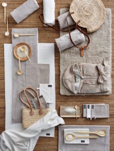 Op een warme bruine ondergrond ligt de Vandyck Toronto-badmat Stone, omringd door neutrale handdoeken en spa-accessoires.