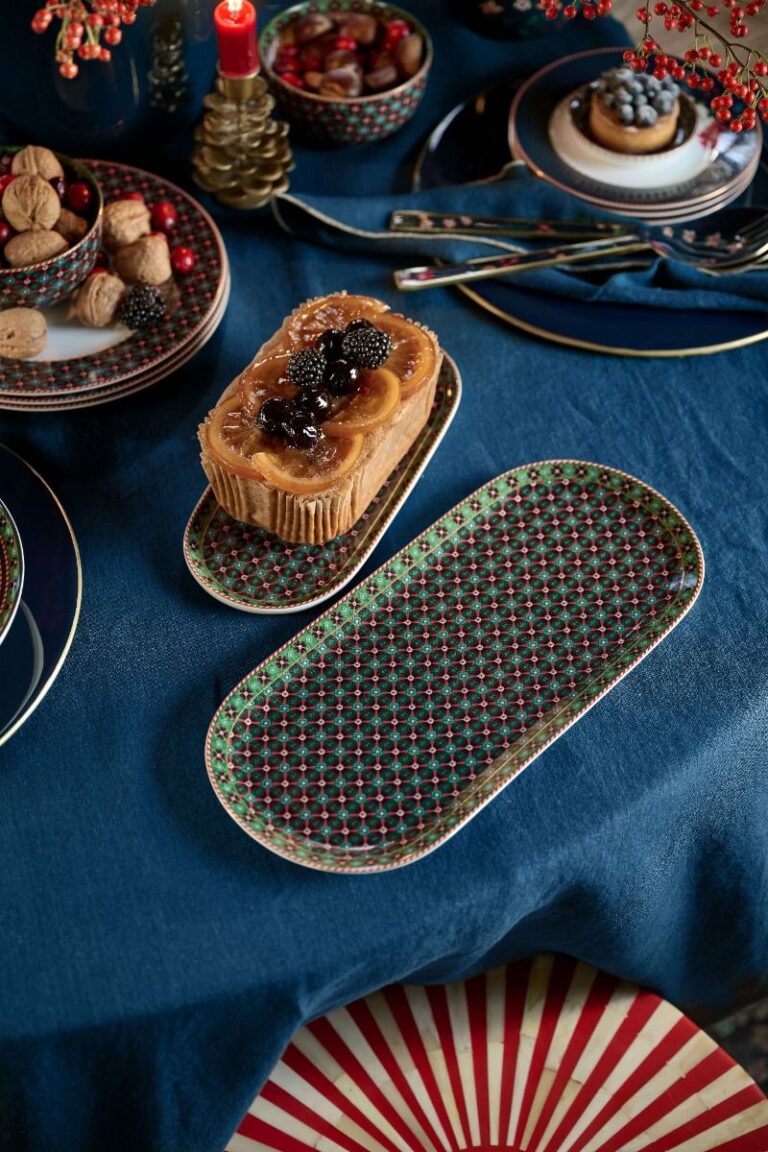 Op een sfeervolle blauwe tafel staan borden uit de Pip Studio-serie met noten, een fruittaart, bestek en een brandende rode kaars.