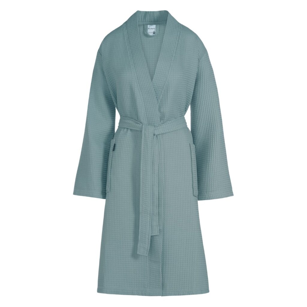 De Vandyck Biarritz nieuwe badjas in mineraalblauw is een badjas met lange mouwen, wafelstructuur, sjaalkraag en bijpassende ceintuur.