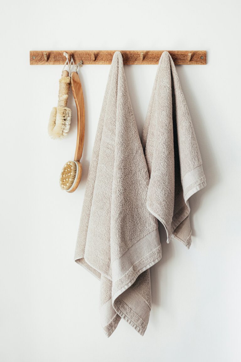 Twee beige handdoeken, net als de beste sportdoeken, hangen aan een houten rek, samen met twee houten badborstels met haren.