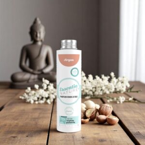 Essentia Wasparfum Argan staat afgebeeld op hout, te midden van witte bloemen en argannoten, met op de achtergrond een vaag boeddhabeeld.