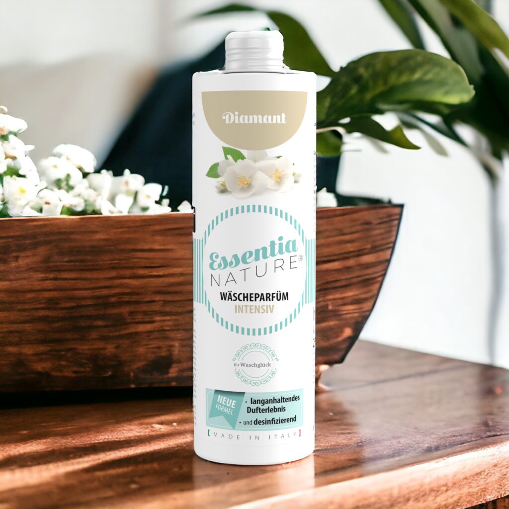 Essentia Wasparfum Diamant, met lichtblauwe details en bloemmotieven, staat op een houten voetstuk tussen witte bloemen en groene bladeren.