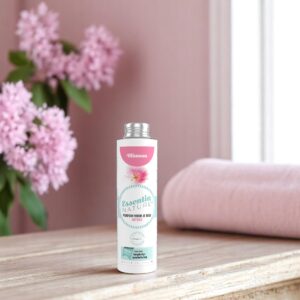 Essentia Wasparfum Mimosa 250 ml staat op een houten ondergrond met zachtroze bloemen en een opgevouwen handdoek op de achtergrond.