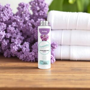 De fles De Essentia Wasparfum Sering van 250 ml staat op een houten voetstuk, omringd door seringenbloemen en stapels zachte witte handdoeken.