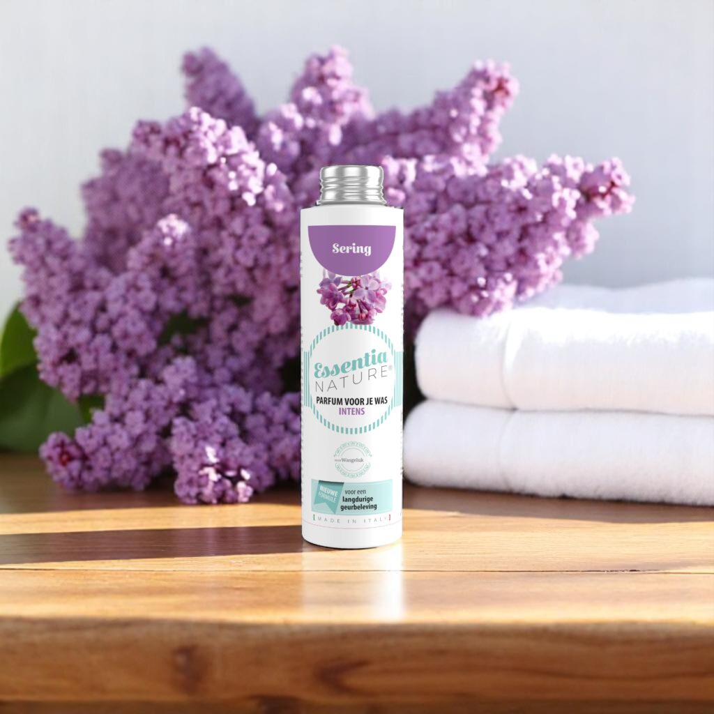 Essentia Wasparfum Sering 250 ml staat op een houten voetstuk met daarachter seringen en twee opgevouwen witte handdoeken; op het etiket staan seringen afgebeeld.