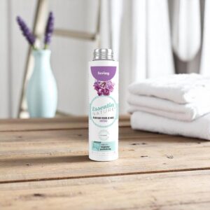 Op een houten tafel staat een flesje Essentia Wasparfum Sering, samen met een opgevouwen witte handdoek en paarse bloemen op de achtergrond.