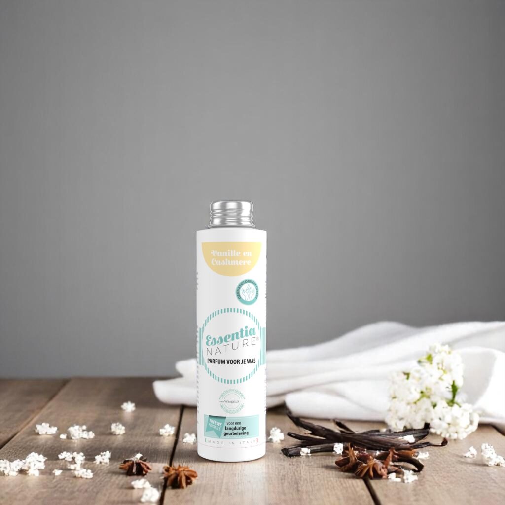 De Essentia-badparfum Vanille en Cashmere 250 ml staat op een houten voetstuk, omringd door vanillestokjes, steranijs, witte bloemen en een handdoek.