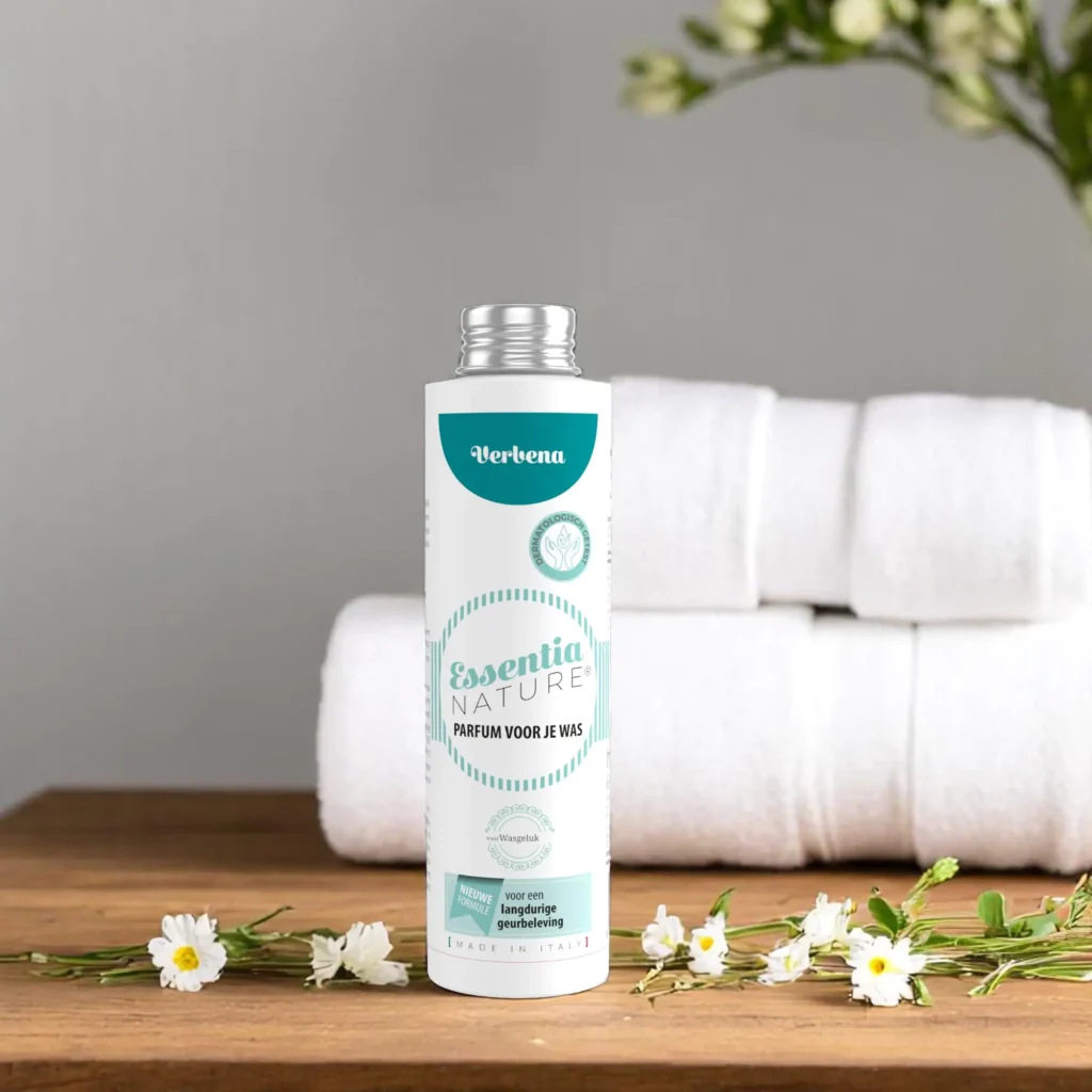 Essentia Waspafurm Verbena 250 ml staat op een houten oppervlak met kleine witte bloemen, opgerolde handdoeken en een grijze bloemenmuur.