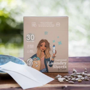 Op een houten ondergrond staat de doos Essentia Wasstrips met een afbeelding van een vrouw en een wasmand, omringd door stenen en wasstrips. Op de verpakking wordt de nadruk gelegd op de milieuvriendelijke en biologische eigenschappen en het aantal wasbeurten.