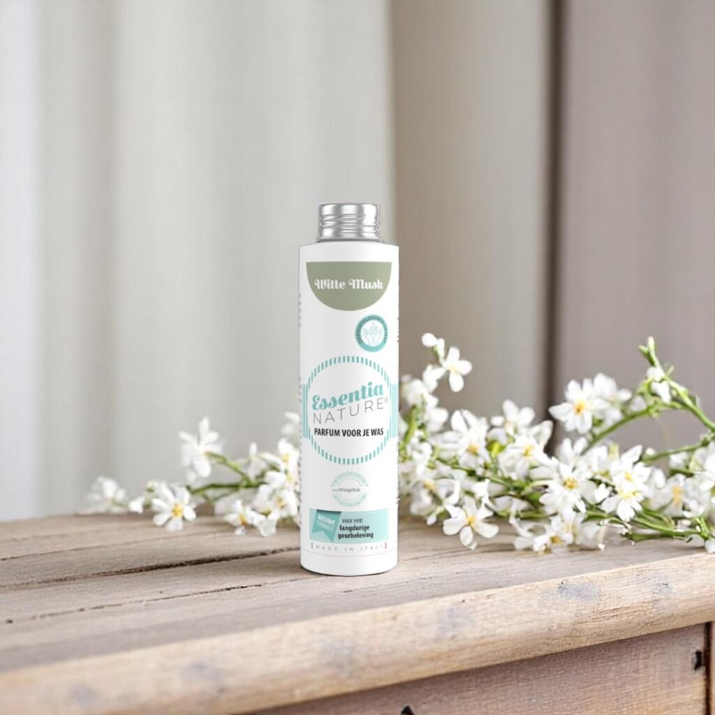 Essentia Wasparfum Witte Musk 250 ml staat op een houten oppervlak naast kleine witte bloemen in een rustige, neutrale omgeving.