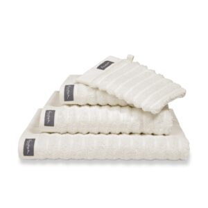 Vier netjes opgevouwen, witte geribbelde Vandyck Home Wave-handdoeken in de kleur Cream Tan, voorzien van een grijs hoeklabel; de kleinste is een bijpassend washandje.