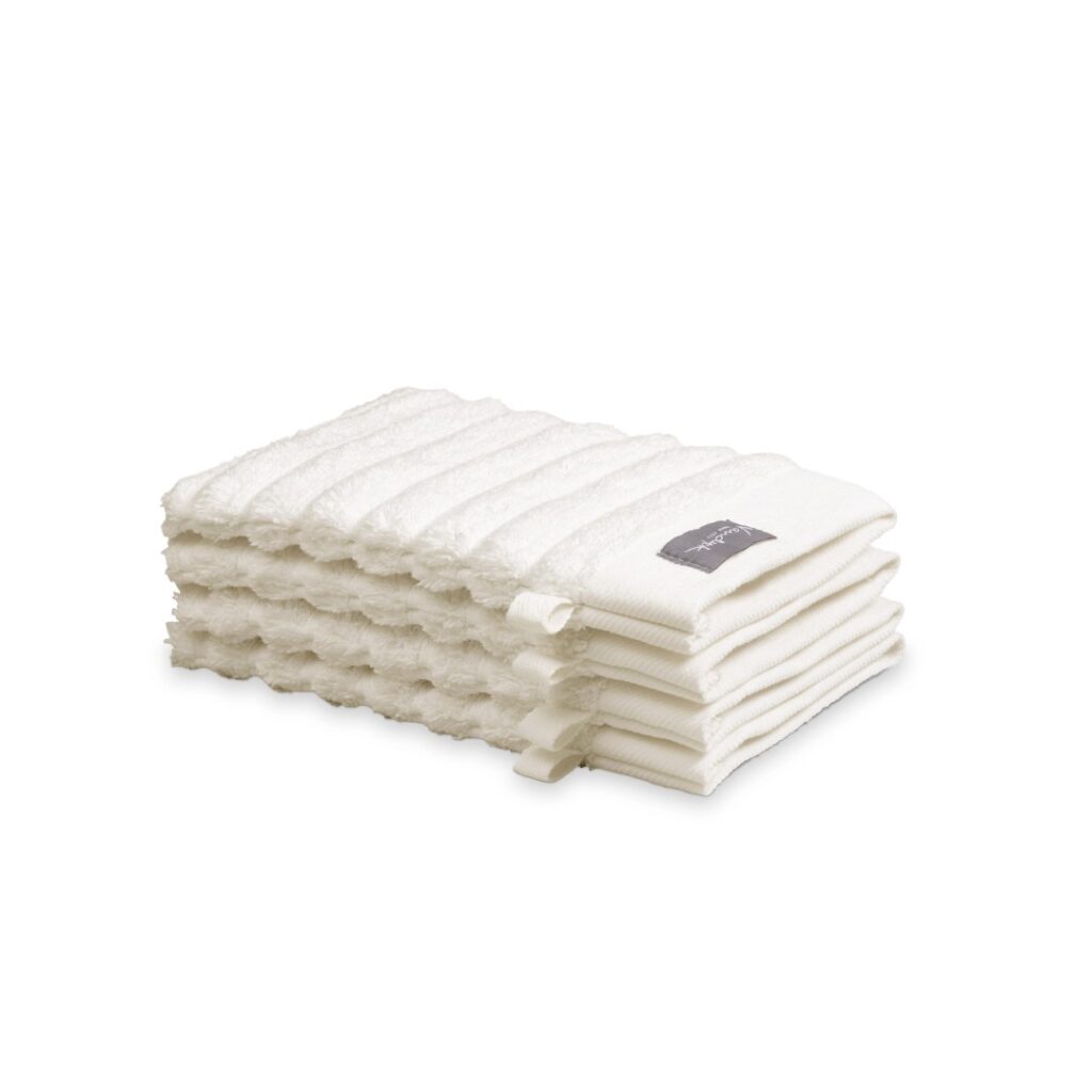 Zes Vandyck Home Wave Washand: crèmekleurige washandjes met een golvend patroon en een stoffen label, netjes opgevouwen.