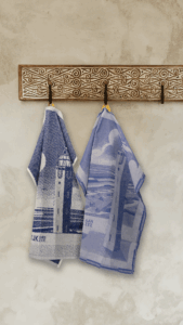 De keukenset Noordwijk aan Zee bestaat uit twee blauw-witte theedoeken met een vuurtoren- en kustmotief, die aan een houten rek tegen een beige muur hangen.