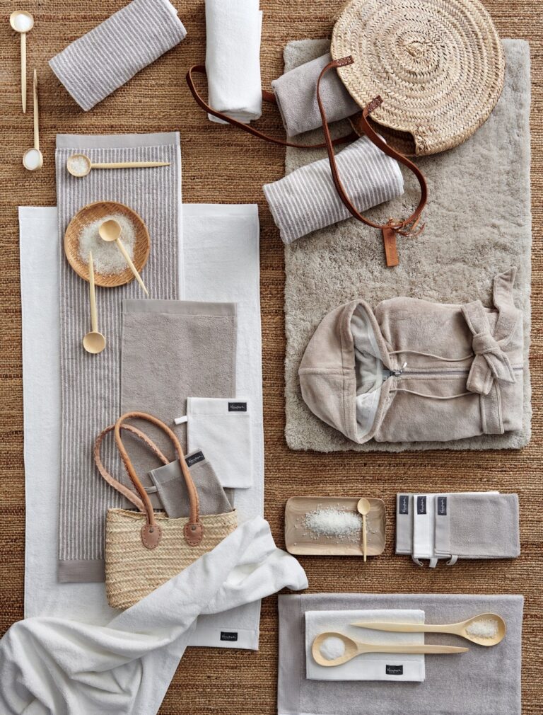 Op een geweven mat liggen handdoeken, washandjes en een badjas sfeervol gerangschikt voor een origineel kerstpakket voor het personeel.