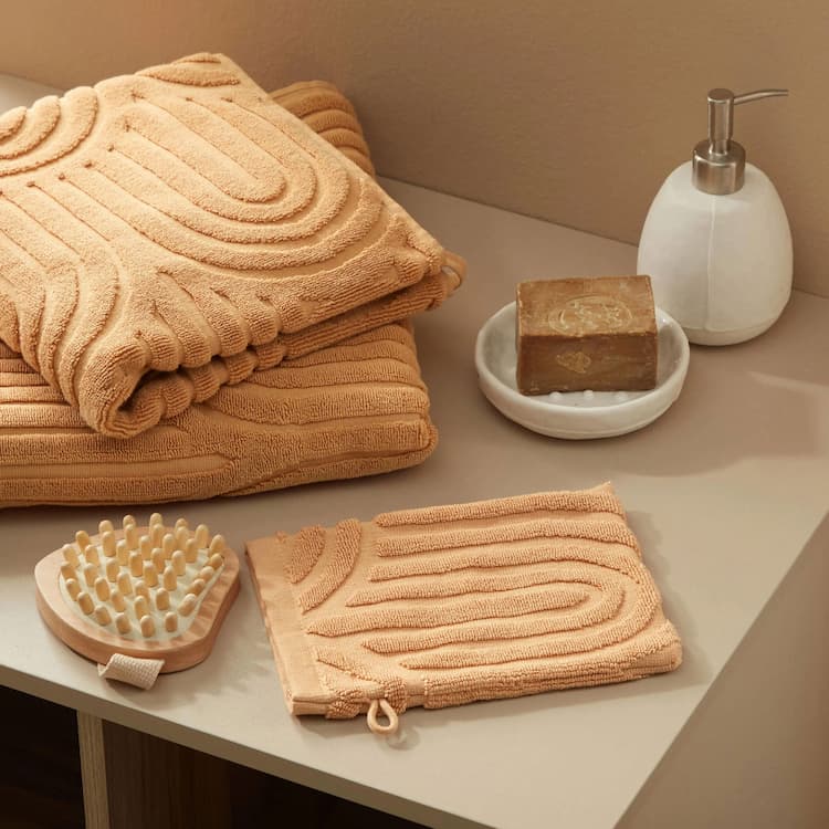 Perzikkleurige handdoeken, een bijpassende washand, een houten massageborstel en een marmeren zeepdispenser zorgen voor spa-luxe op het werk.