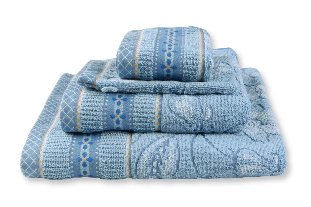 De Pip Studio Jasmin Jacquard-badhanddoeken in lichtblauw liggen netjes opgestapeld, met strepen, stippen en bloemmotieven op elke handdoek.
