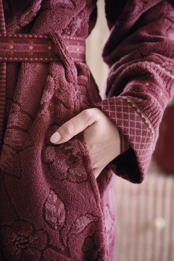 Iemand draagt de Pip Studio Jasmin Jacquard-badjas in donkerroze, met de rechterhand in de zak, en laat de jacquard-bloemenmanchet zien.