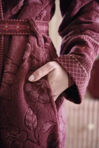 Iemand draagt de Pip Studio Jasmin Jacquard-badjas in donkerroze, maat S, en laat zijn hand ontspannen in de zak van de badjas rusten.