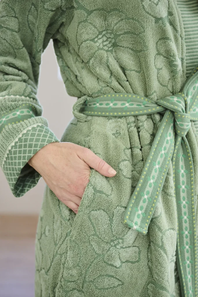 Een persoon poseert met één hand in de zak en draagt de Pip Studio Jasmin Jacquard-badjas in groen, maat XXL, met bijpassende ceintuur, waarbij het subtiele bloemenpatroon mooi tot zijn recht komt.