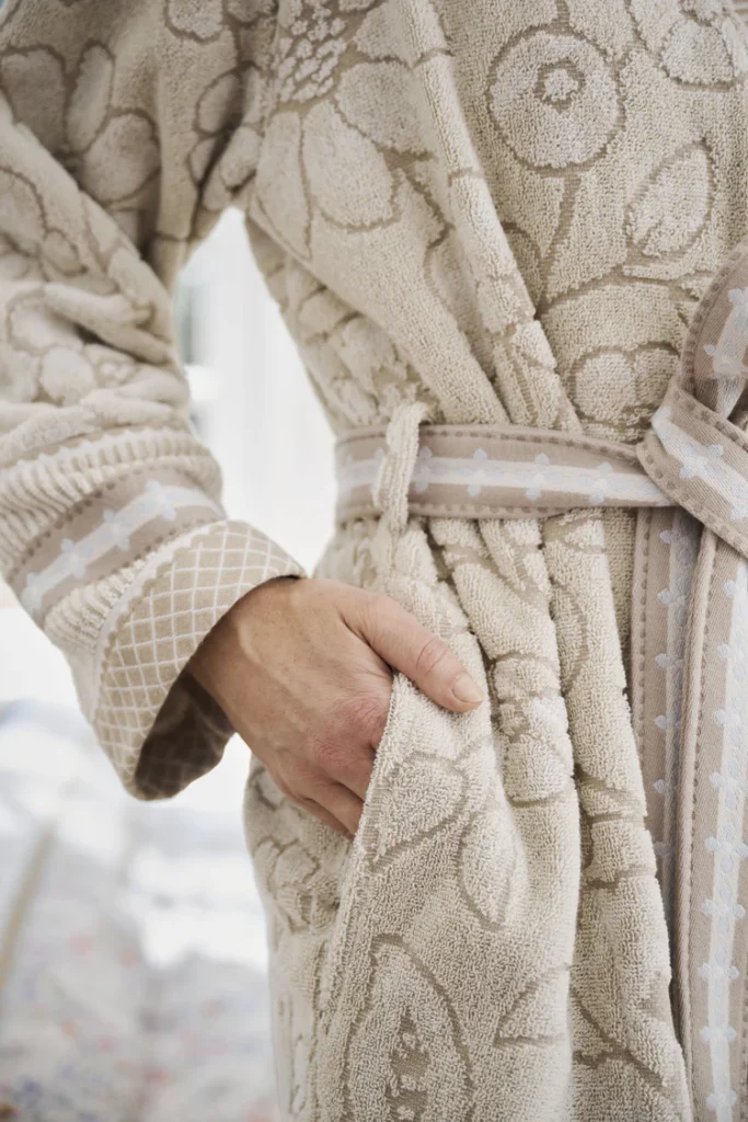 Een persoon draagt de Pip Studio Jasmin Jacquard-badjas in de kleur Sand, maat L, een beige badjas met bloemenpatroon en ceintuur, en heeft één hand in de zak.