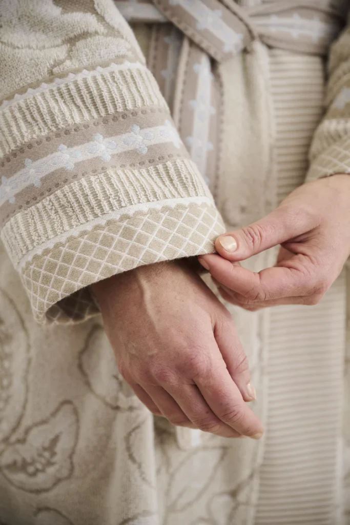 Een close-up van handen die de mouw van de Pip Studio Jasmin Jacquard-badjas Sand L in beige en crème met reliëfpatronen recht trekken.