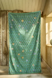 In een zonnige, rustieke kamer met houten vloeren en een houten deur ligt het Pip Studio Sea Dots-strandlaken in groen met blauwe cirkels en kleurrijke bloemenpatronen.
