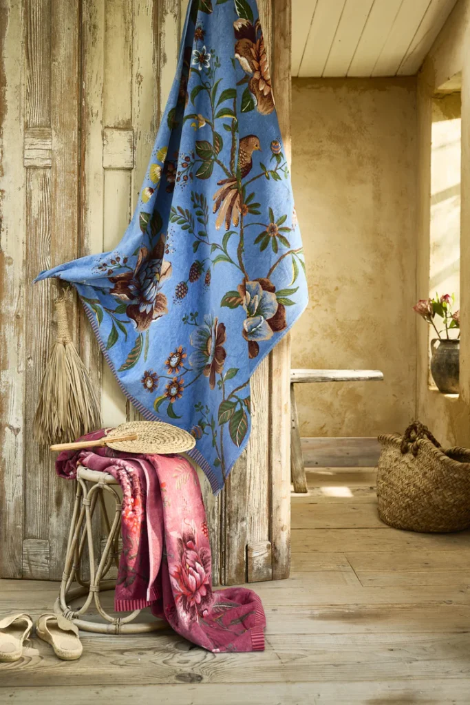 In een rustieke kamer met verweerd hout ligt het Pip Studio Secret Garden strandlaken Blue als een bloemrijke deken in zacht licht.