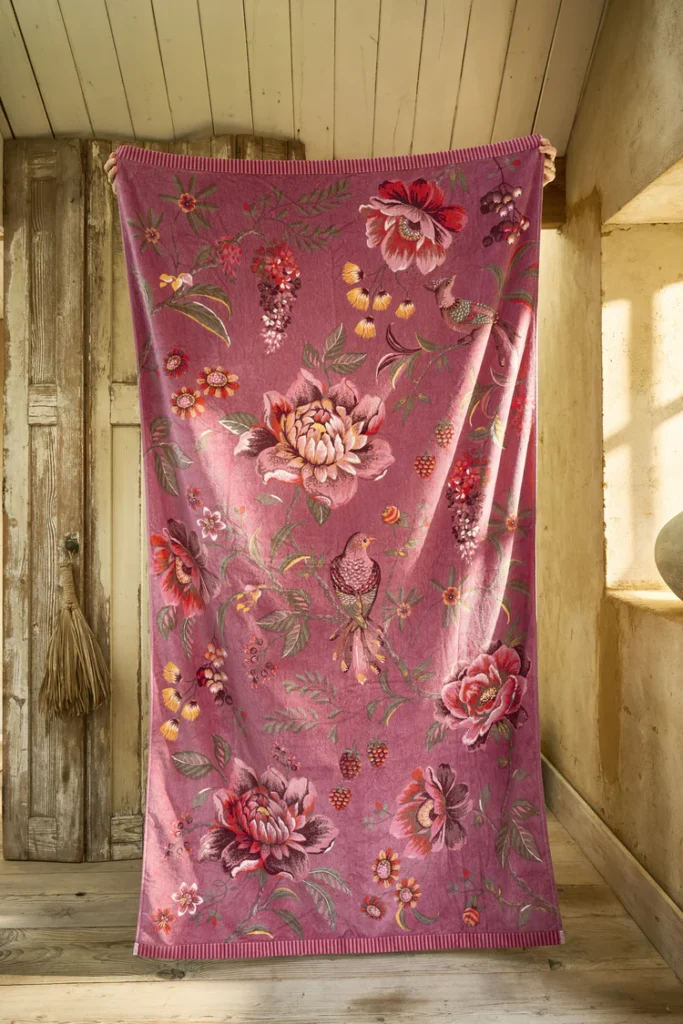 Het Pip Studio Secret Garden-strandlaken in roze met grote bloemen, bessen, bladeren en een vogeltje hangt in een zonnige kamer.