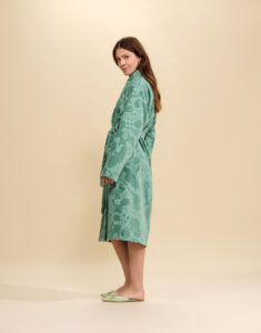 Vrouw draagt een groene badjas met bloemmotief en een ceintuur, tot kniehoogte, gecombineerd met lichtgroene slippers
