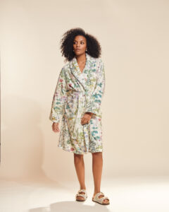 Vrouw draagt een witte badjas met botanische bloemenprint, geknoopt op taille, gecombineerd met gevlochten sandalen