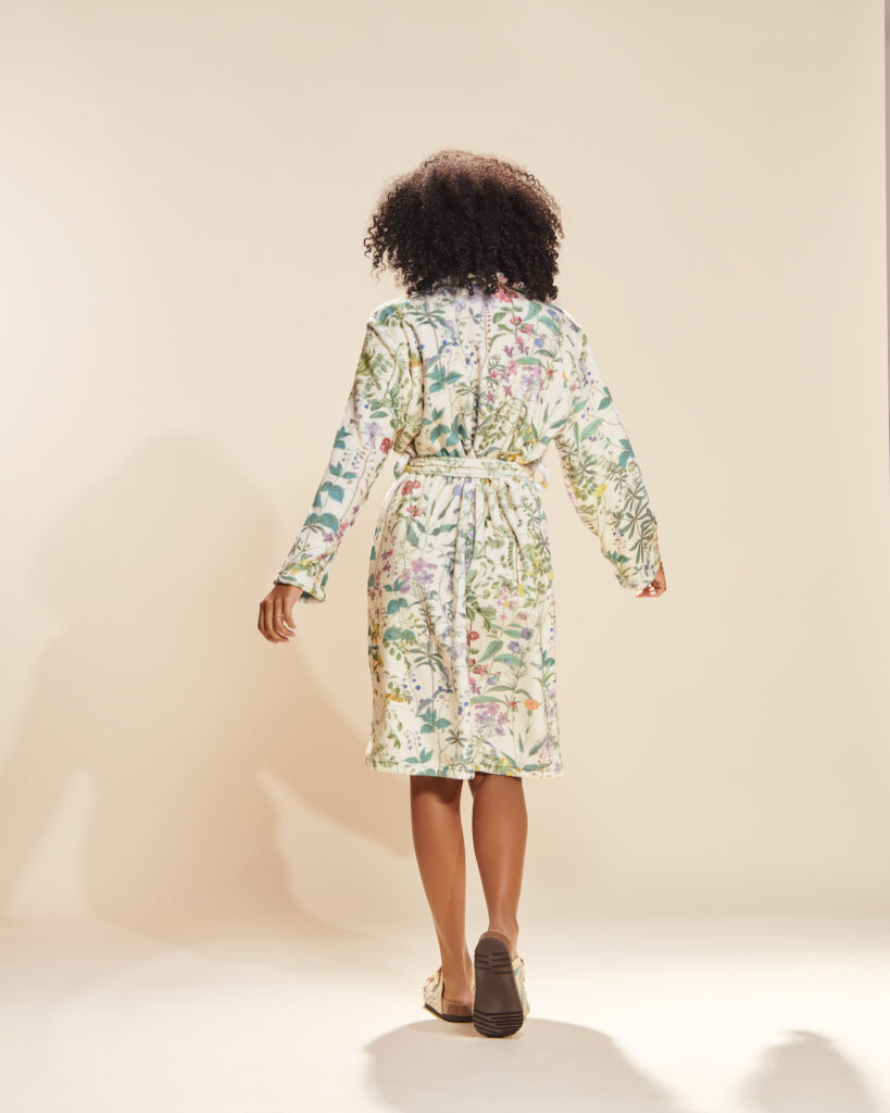 Achterkant van een midi-jurk met botanische bloemenprint, strikceintuur en lange mouwen, gedragen door een vrouw